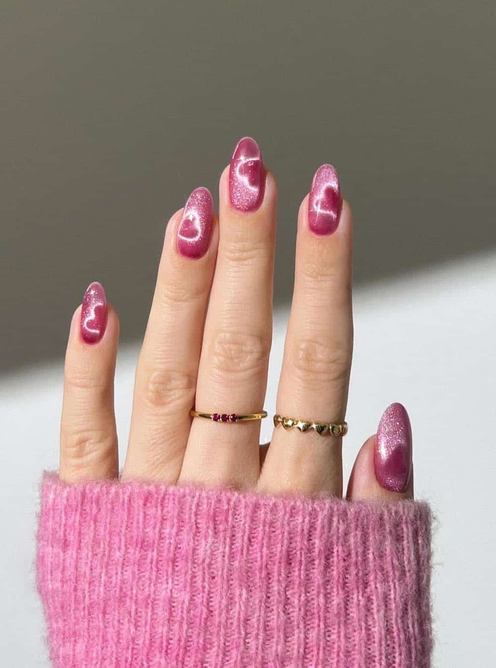 A hand with medium almond nails painted with shimmering pink velvet polish with heart outlines
