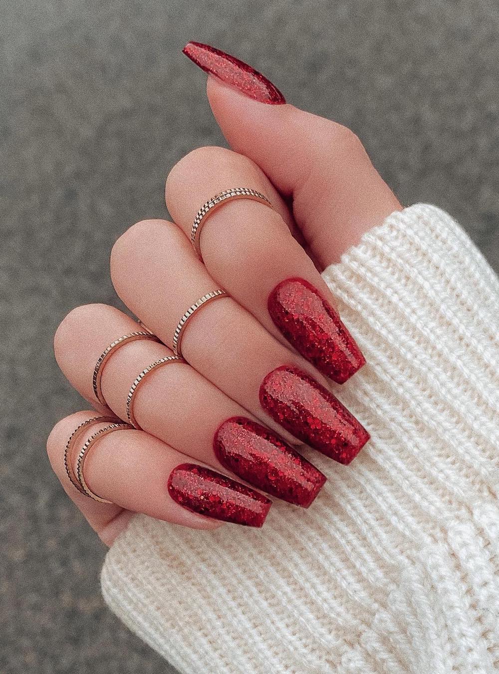A hand with long coffin nails painted with chunky red glitter polish