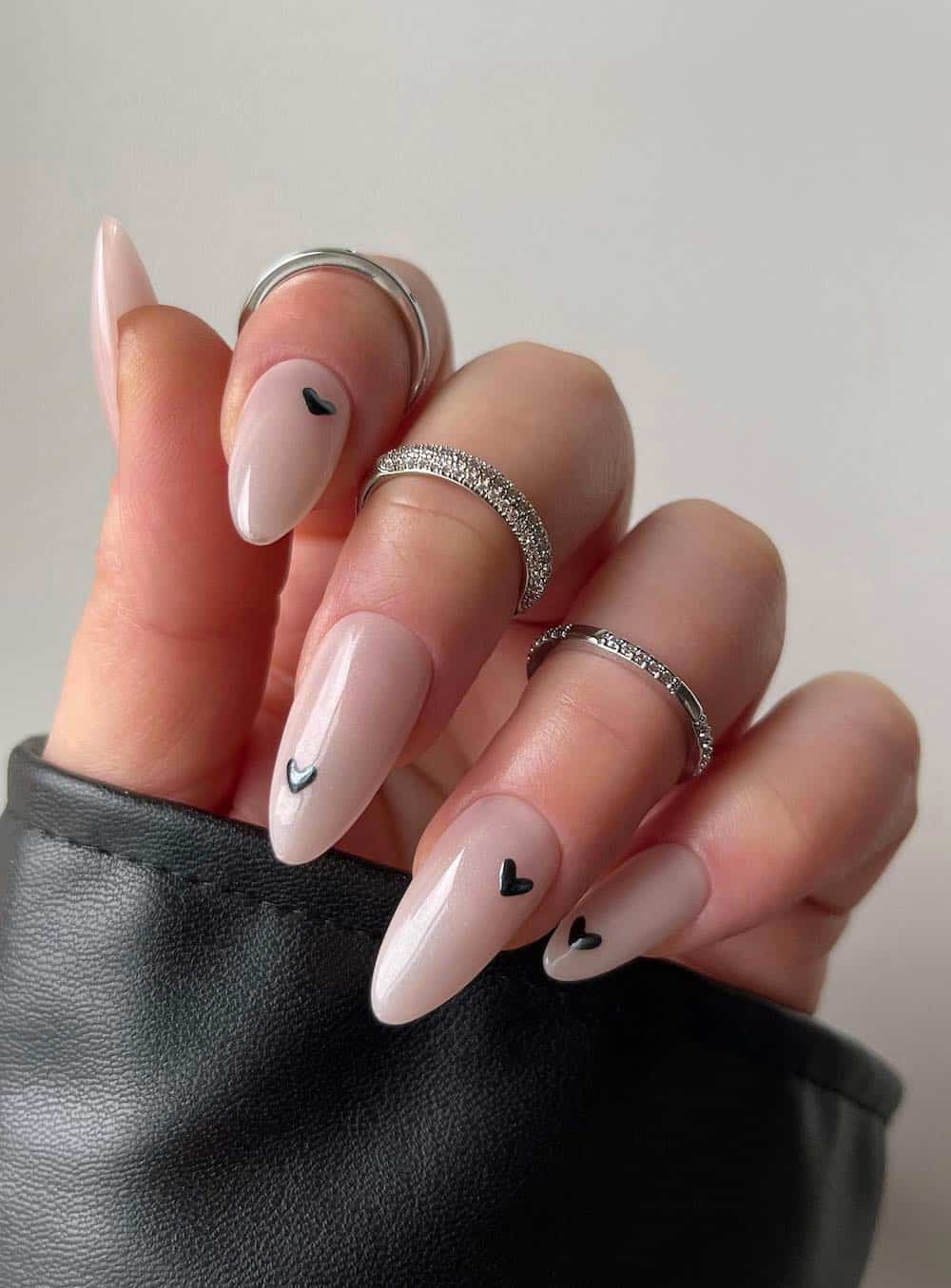 A hand with long almond nails painted a milky white with black heart details