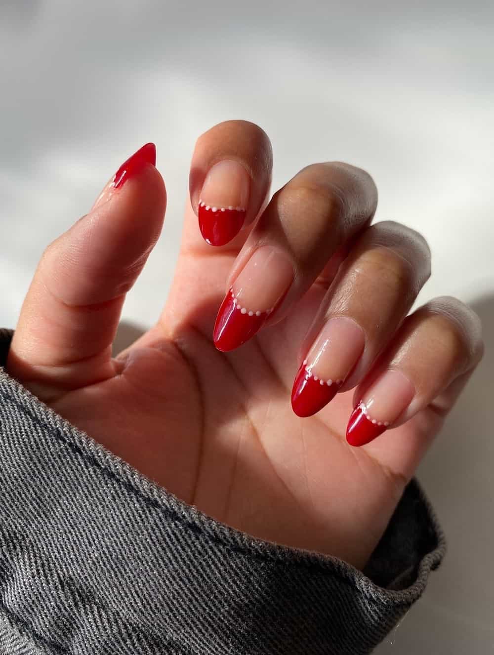 A hand with long almond nails painted with red French tips and lined with white dots