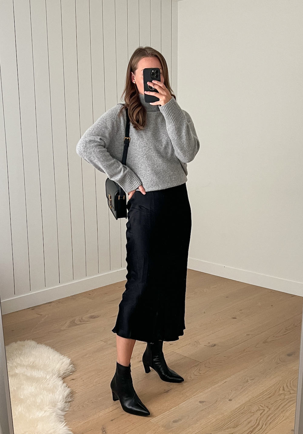 Christal wearing a black slip skirt with black booties and a grey sweater.