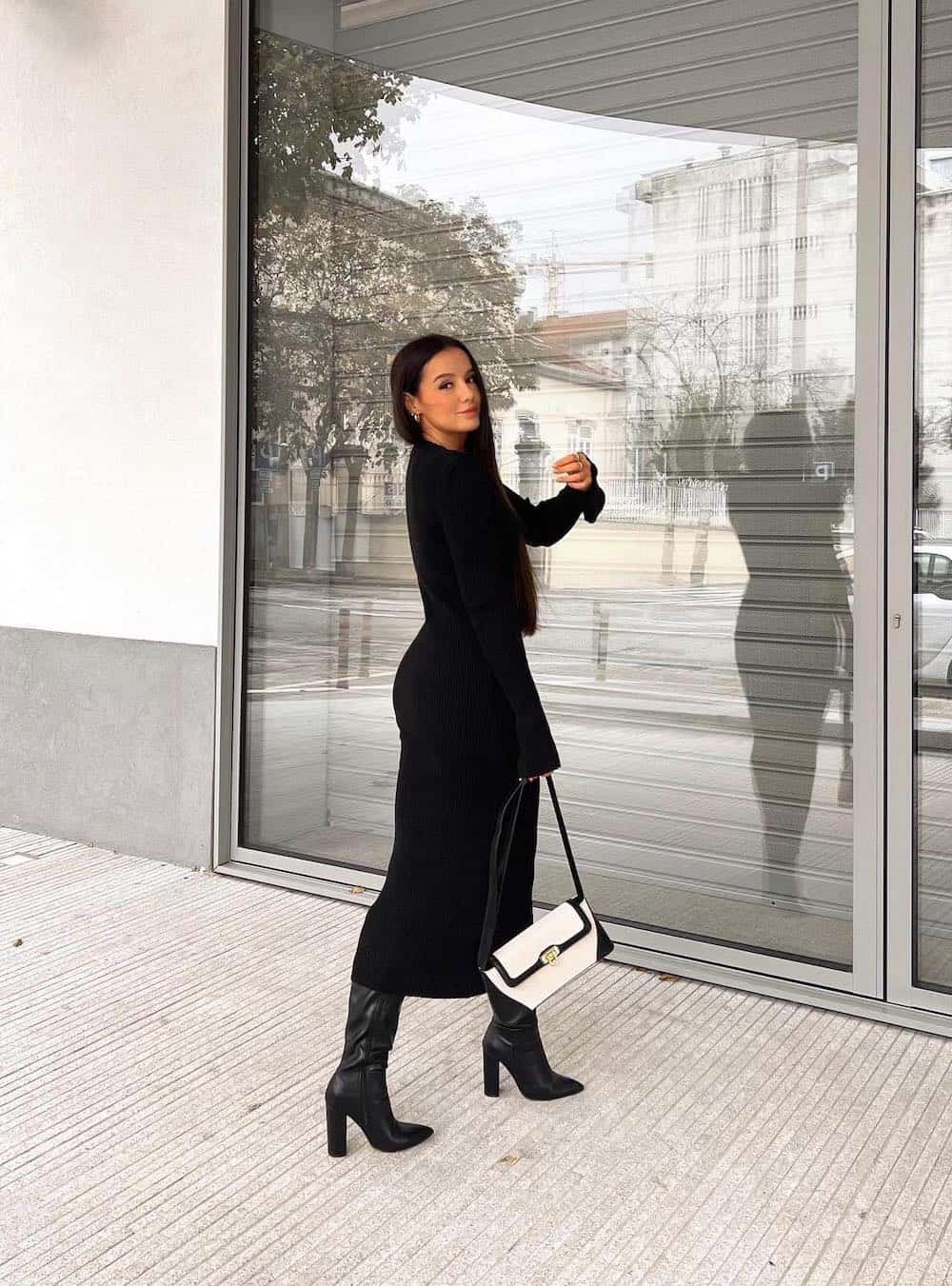 Woman wearing tall black boots with a black midi length sweater dress.