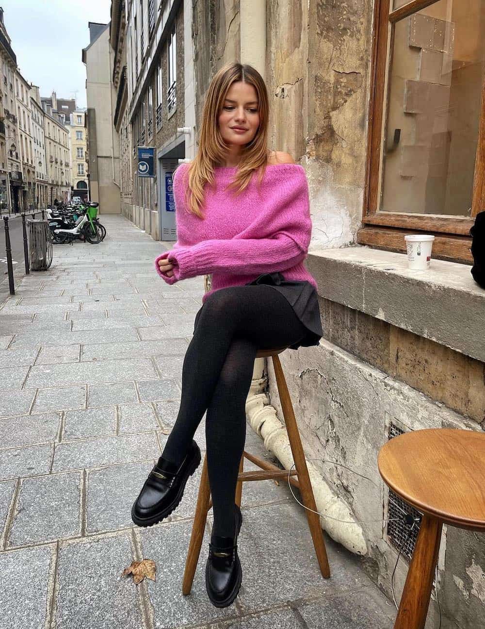 Woman wearing a black skirt with loafers and a pink sweater.