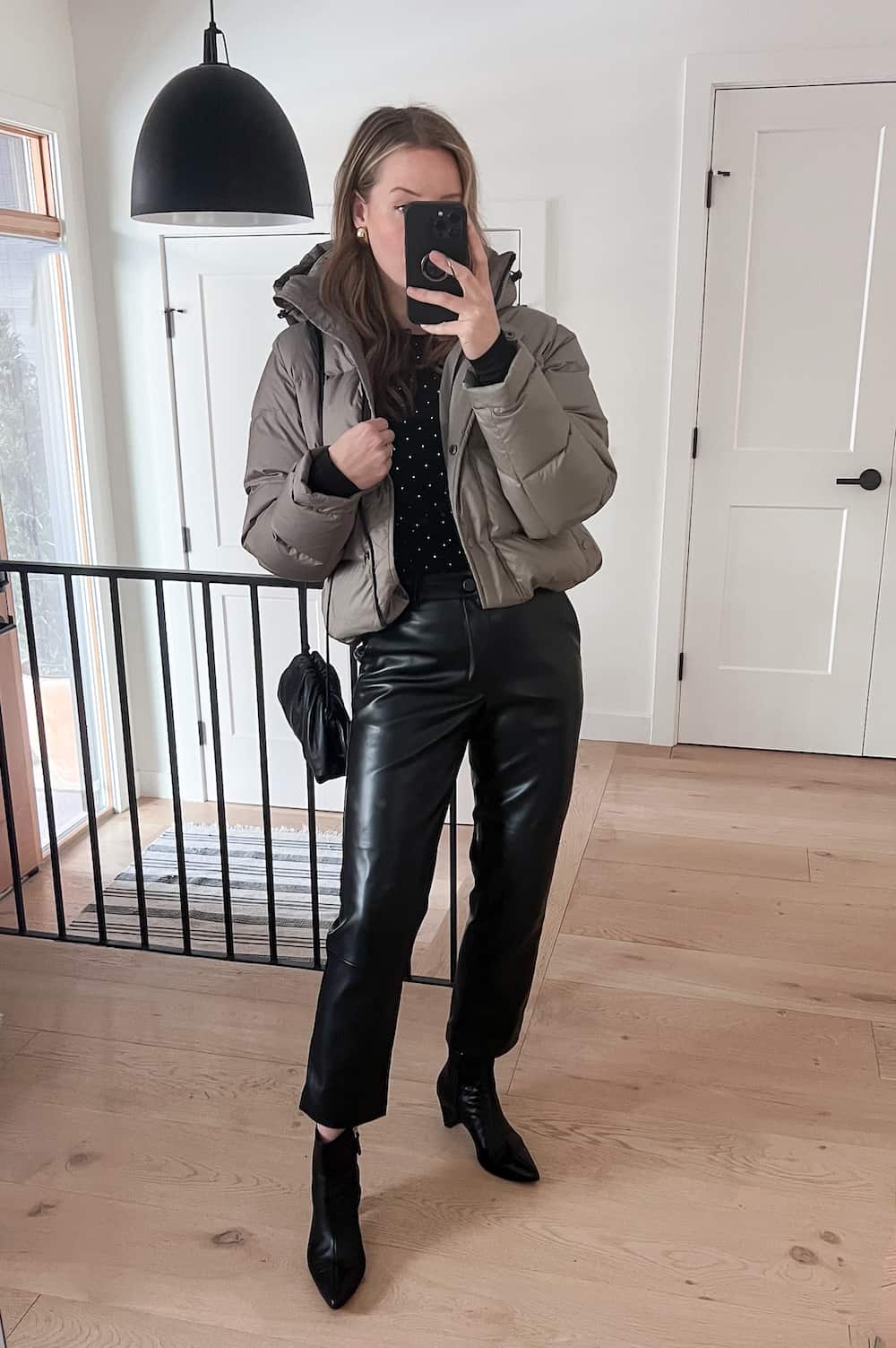 woman wearing a winter going out outfit with a taupe cropped puffer jacket, black leather pants, and black ankle boots