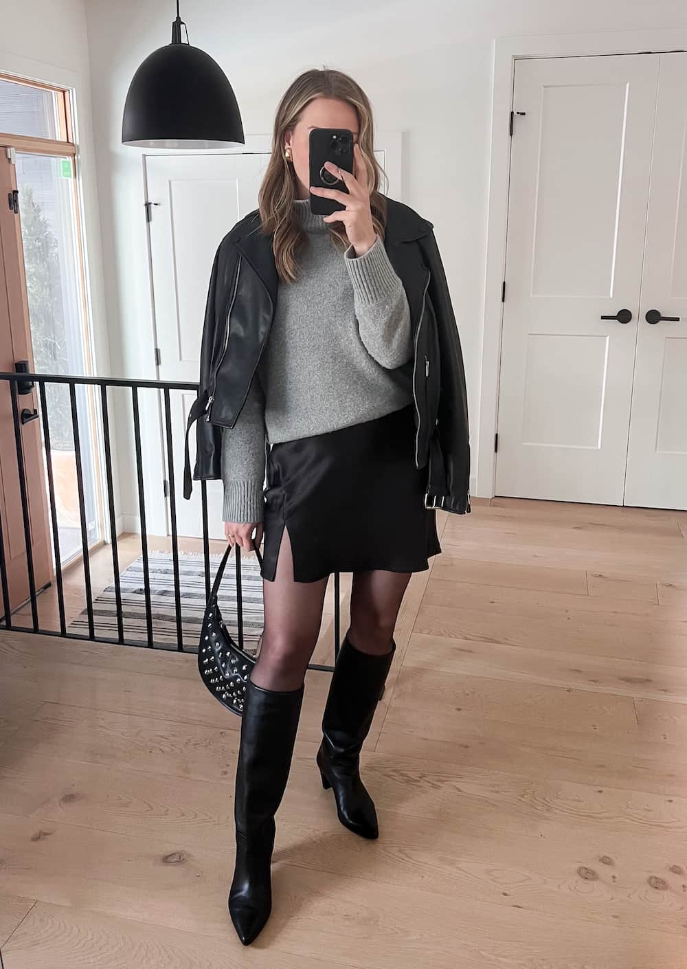 woman wearing a winter going out outfit with a black leather jacket over a grey knit turtleneck, black mini skirt, tights, and black knee-high boots