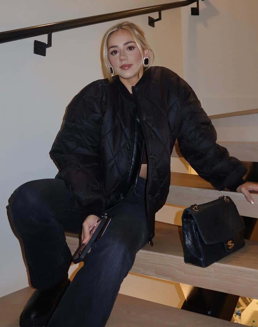 woman wearing a winter going out outfit with a black puffer bomber jacket cropped black top, black jeans, and lug boots