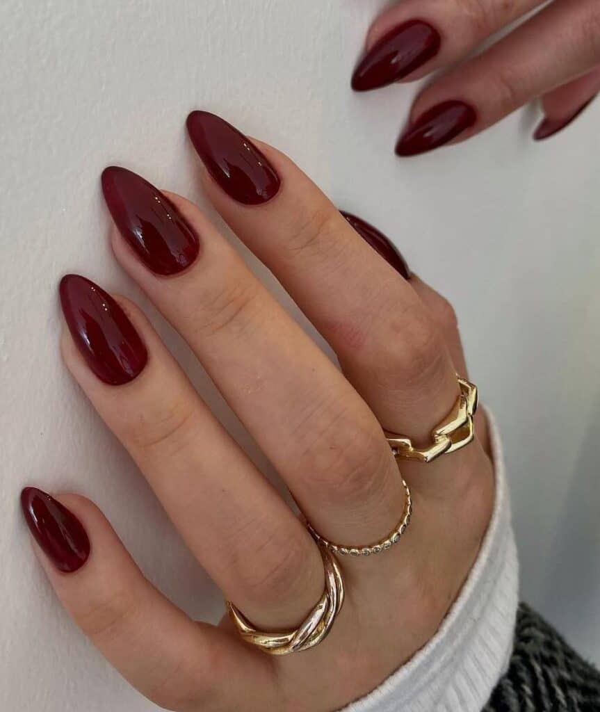 A hand with medium almond nails painted a glossy burgundy-red