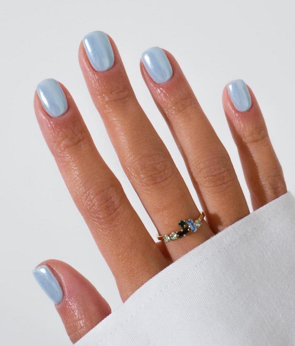 A hand with short squoval nails painted an icy blue with a chrome finish