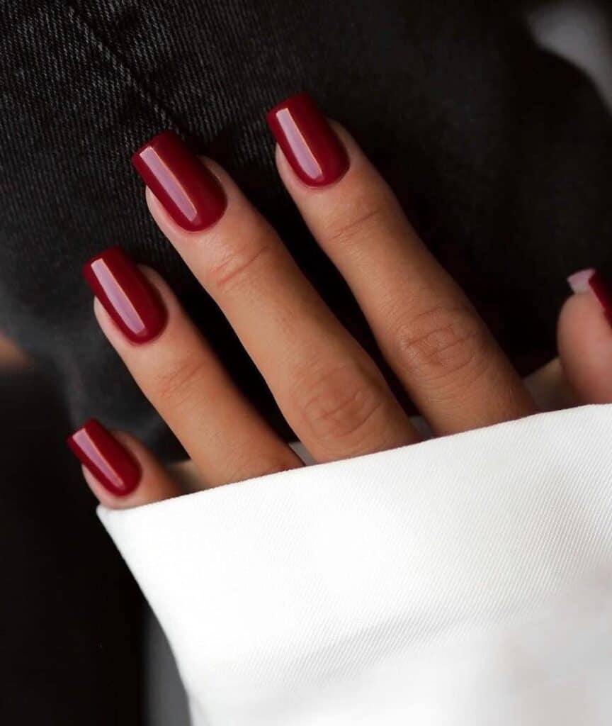 A hand with medium square nails painted in glossy wine red polish