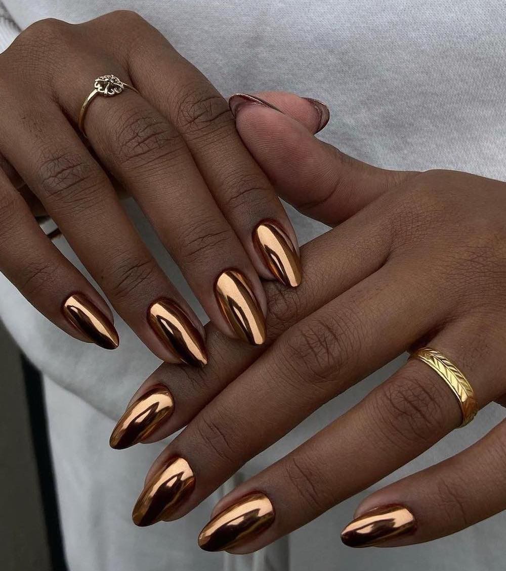 A hand with medium almond nails painted in a gold chrome