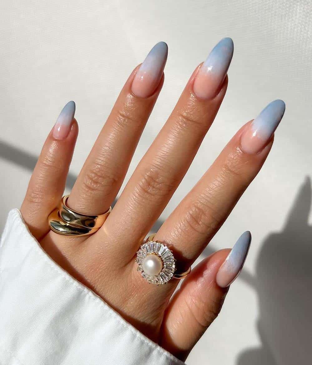 A hand with long almond nails painted an icy blue to nude pink ombre