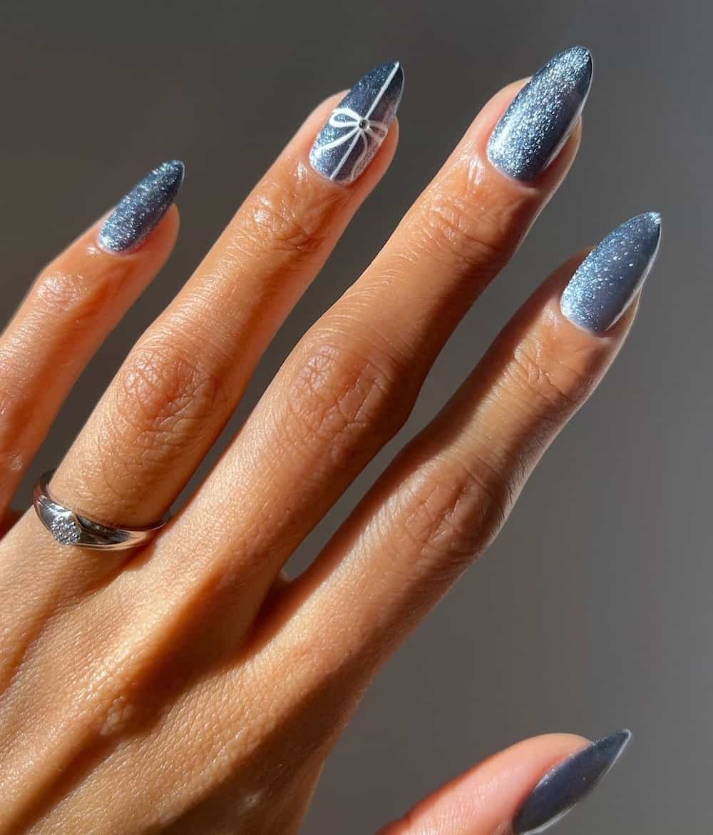 A hand with medium almond nails painted a shimmering icy blue with a white bow detail