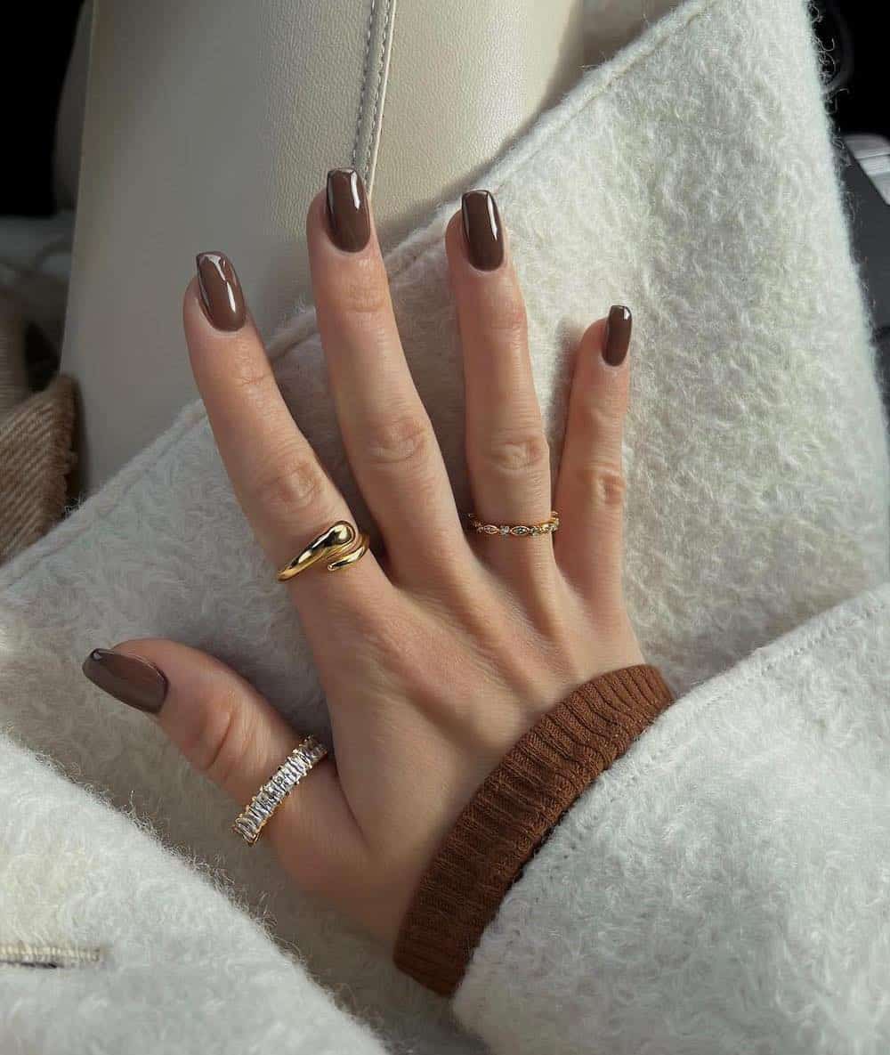 A hand with medium square nails painted a dark brown with a glossy finish