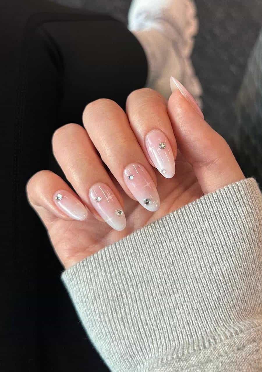 Medium almond nails with a soft pink and white ombre, white sparkles, and silver gem details