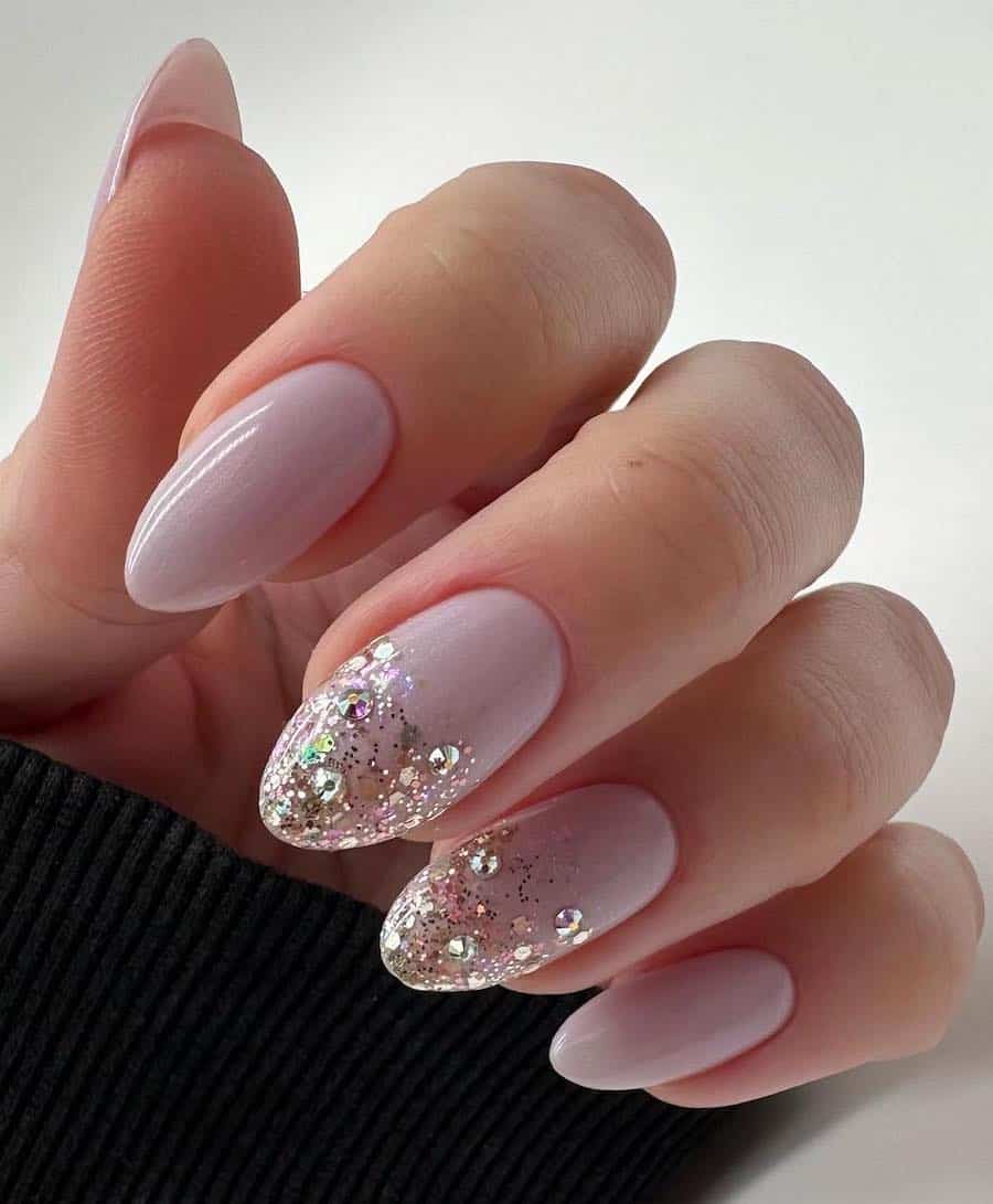 Medium almond nails with pastel pink polish and two nails with chunky glitter ombre tips