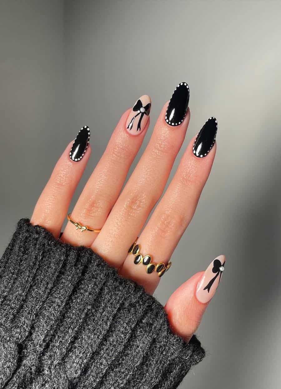 Medium almond nails with black light nails bordered with white dots and two light beige accent nails with black bows and pearl details