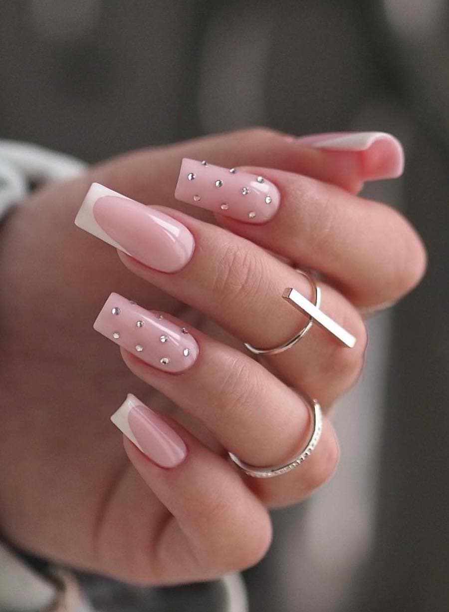 Long square nails painted a soft pink with white tips and two accent nails with crystals