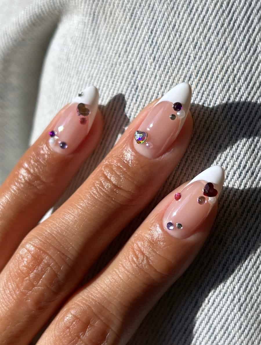 Short glossy nude almond nails with white tips, silver crystals, and iridescent heart gems