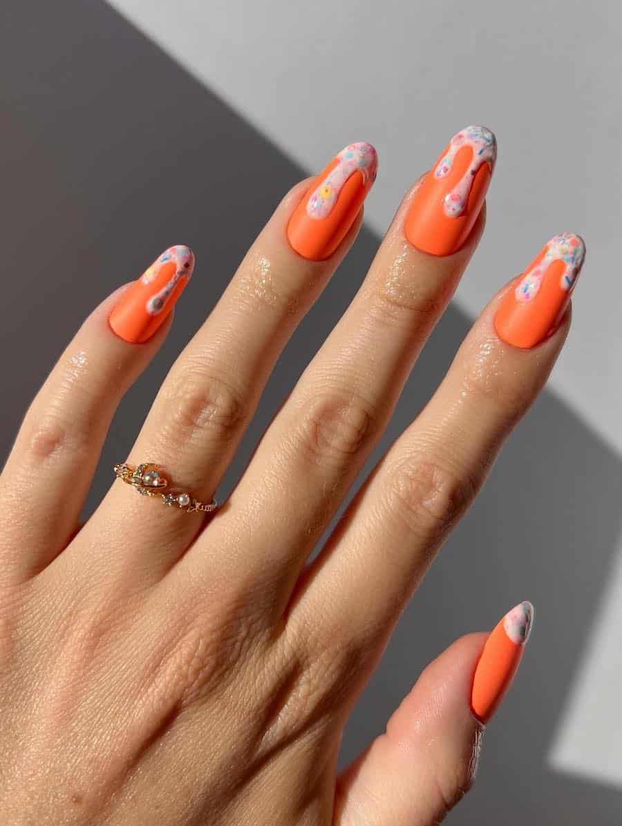 Medium round nails with a bright orange polish and light pink dripping tips with colorful confetti