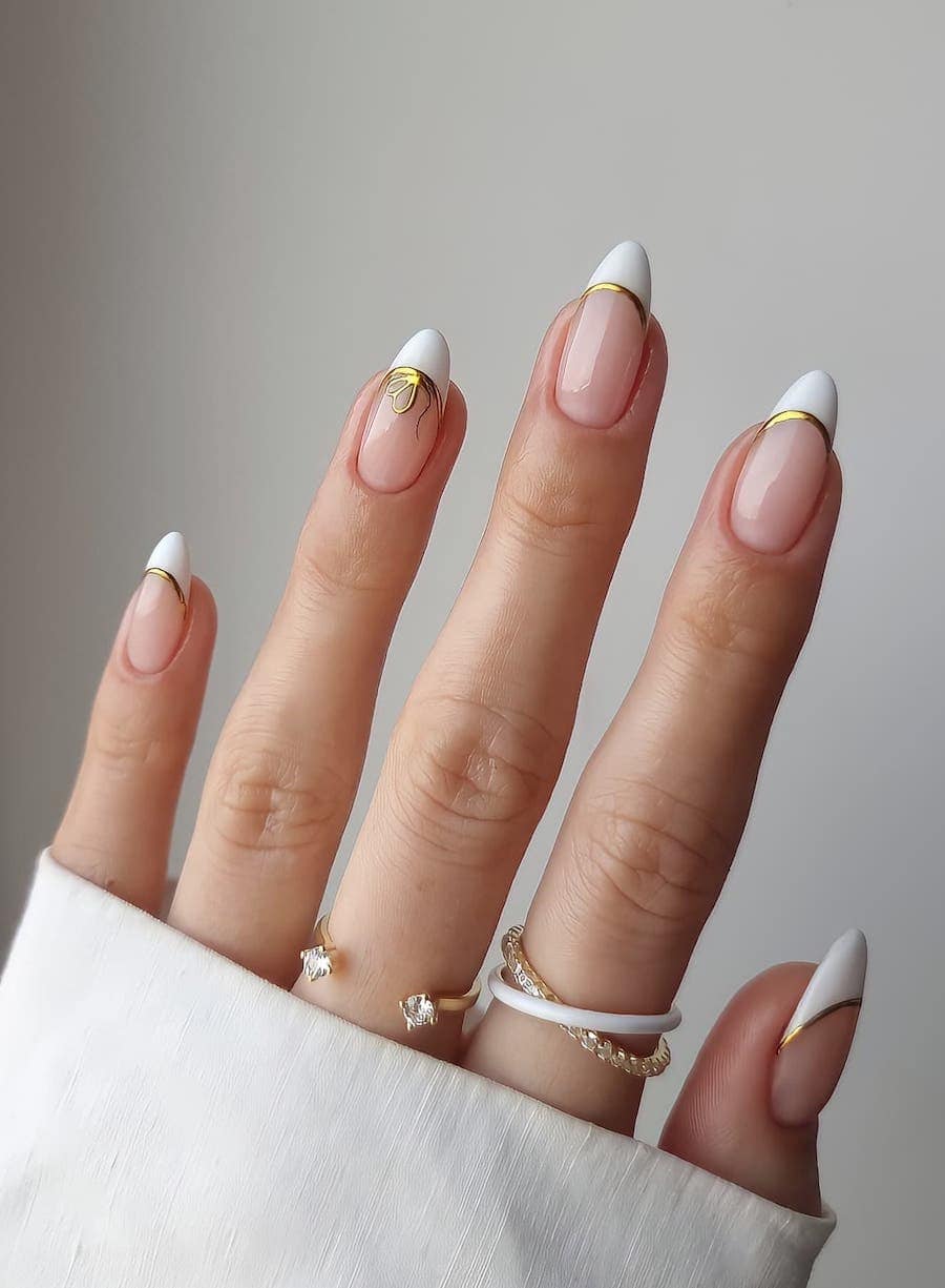 Medium glossy nude almond nails with white tips, gold borders, and one accent nail with a gold bow detail