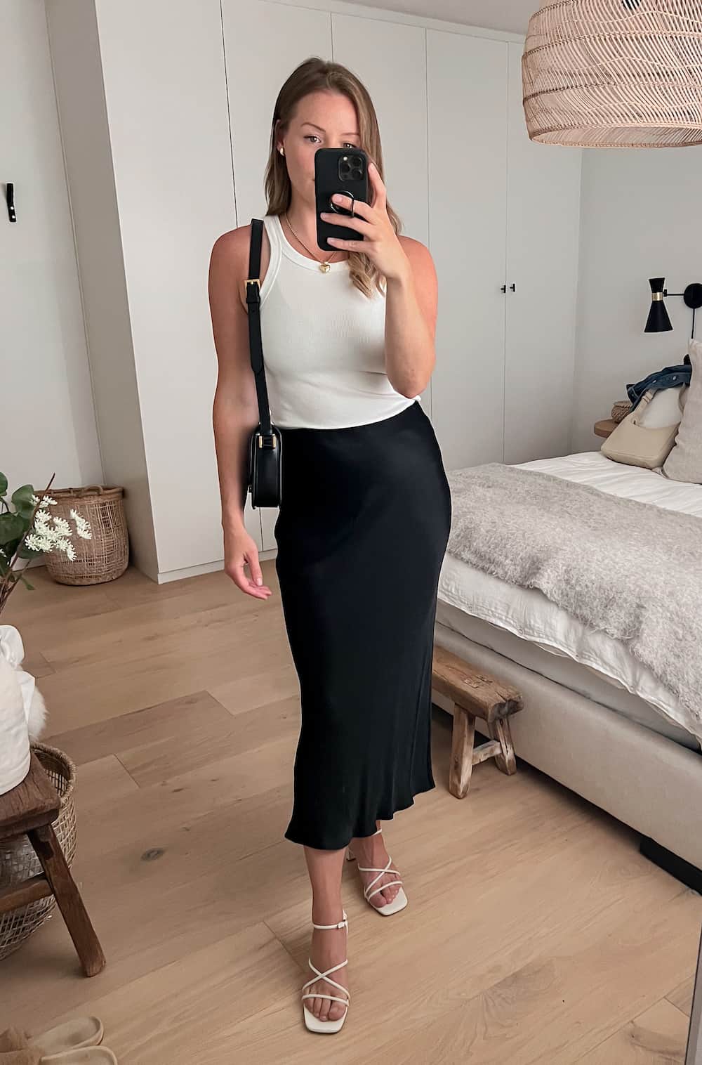 Christal wearing a black slip skirt with a white tank top and white strappy heels.
