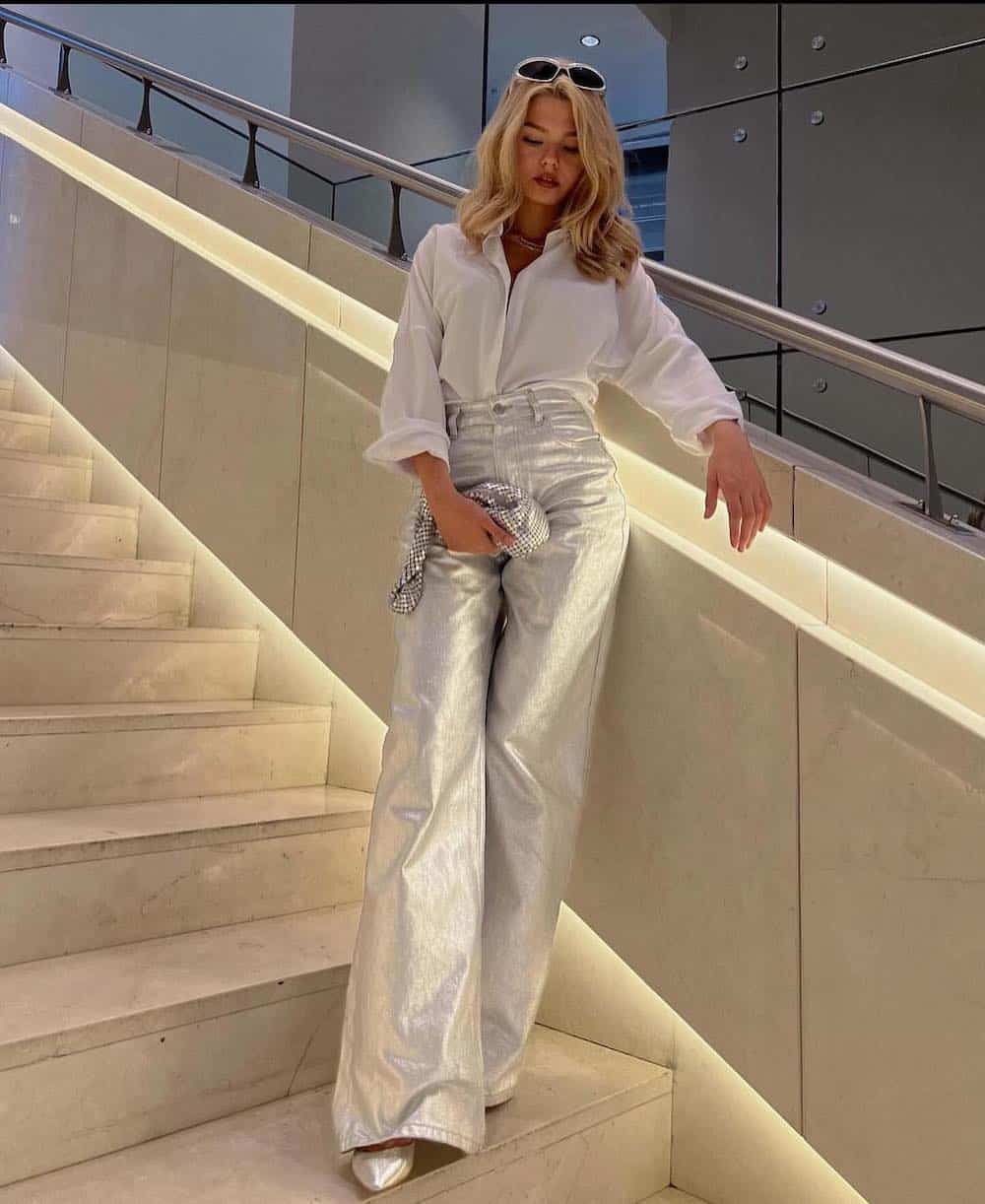 Woman wearing silver wide leg jeans with silver pointed toe shoes, and a white button up.