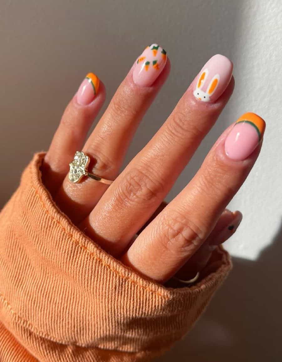 Short nude pink squoval nails with orange and green French tips, a peekaboo bunny, and carrot nail art