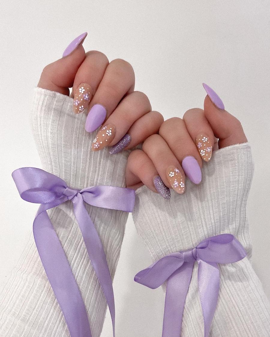 Long almond nails painted light purple and glitter purple with beige accent nails featuring floral art