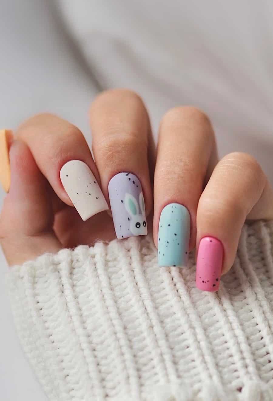 Long square nails in pastel gradient colors with black speckles, a matte finish, and bunny nail art