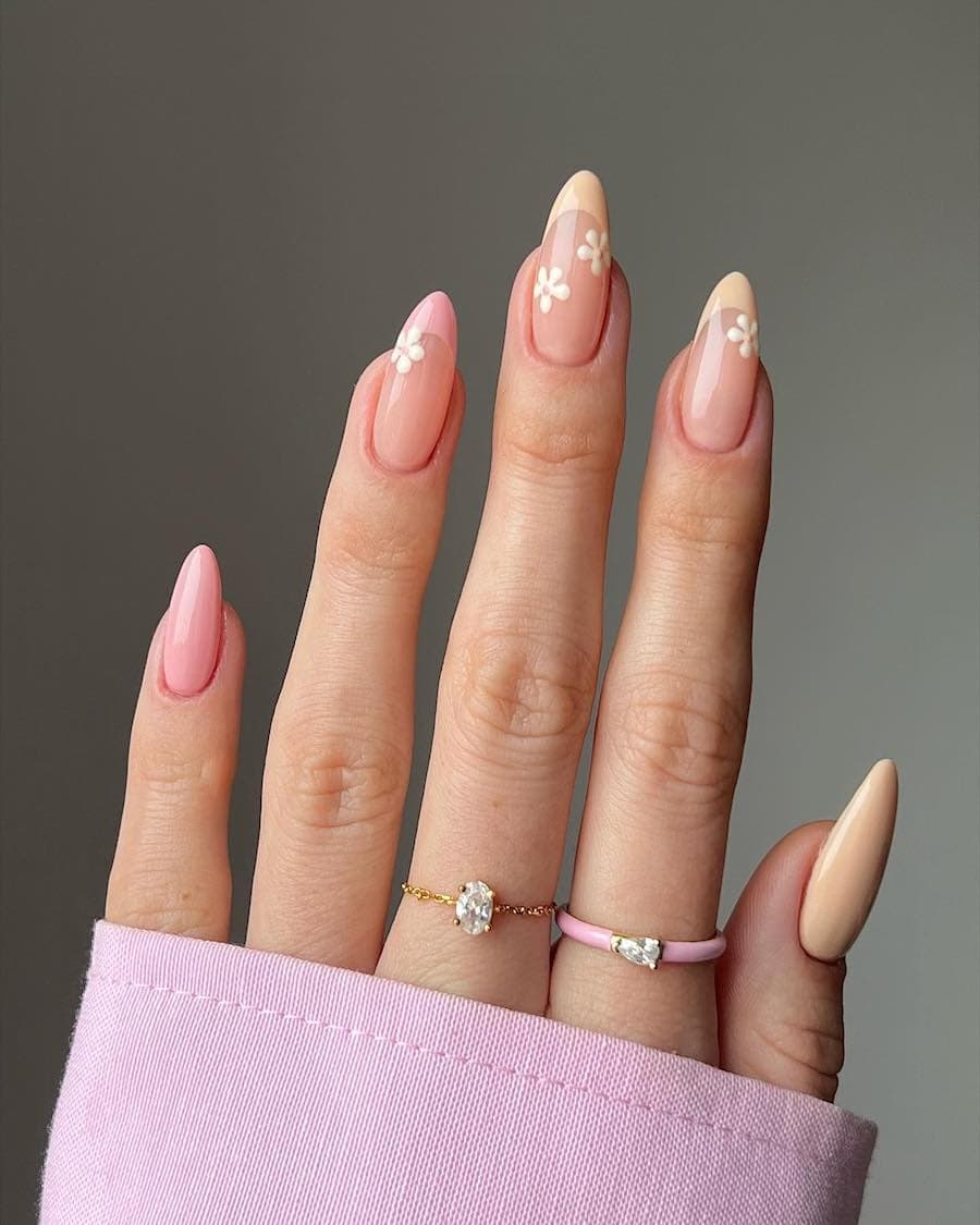 Long nude almond nails with peach and pink nail polish featuring French tips with white flowers and solid-colored nails