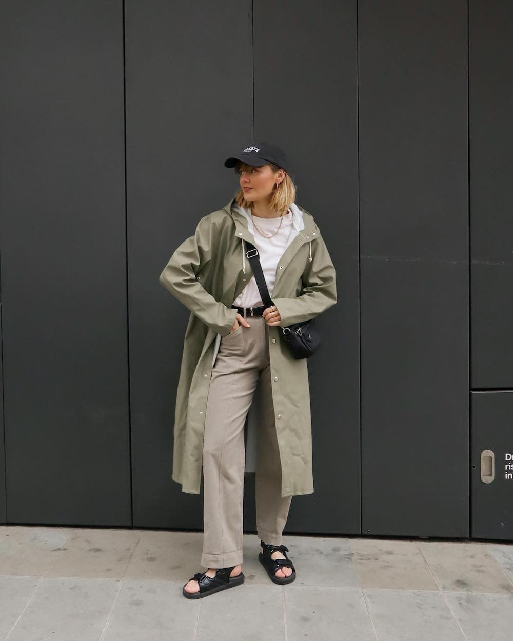 Woman wearing tan trousers, Birkenstock sandals, a white t-shirt and a green trench raincoat.