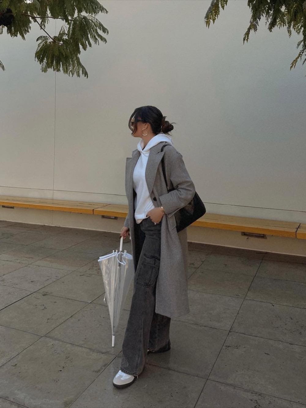 Woman wearing cargo pants, sneakers, a white hoodie and a grey trench coat.