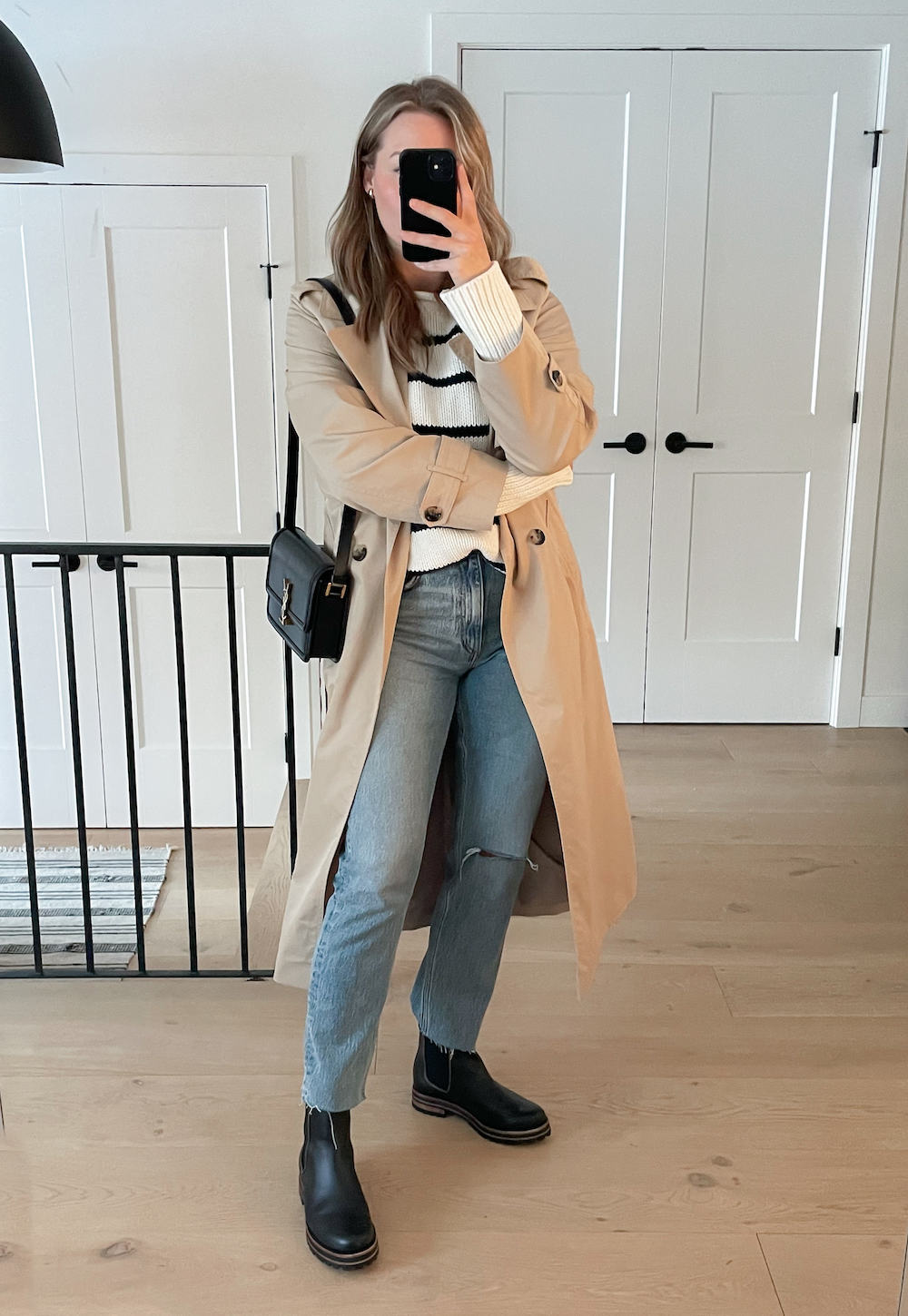 Christal wearing straight jeans with black Chelsea boots, a black and white stripped sweater and a tan trench coat.