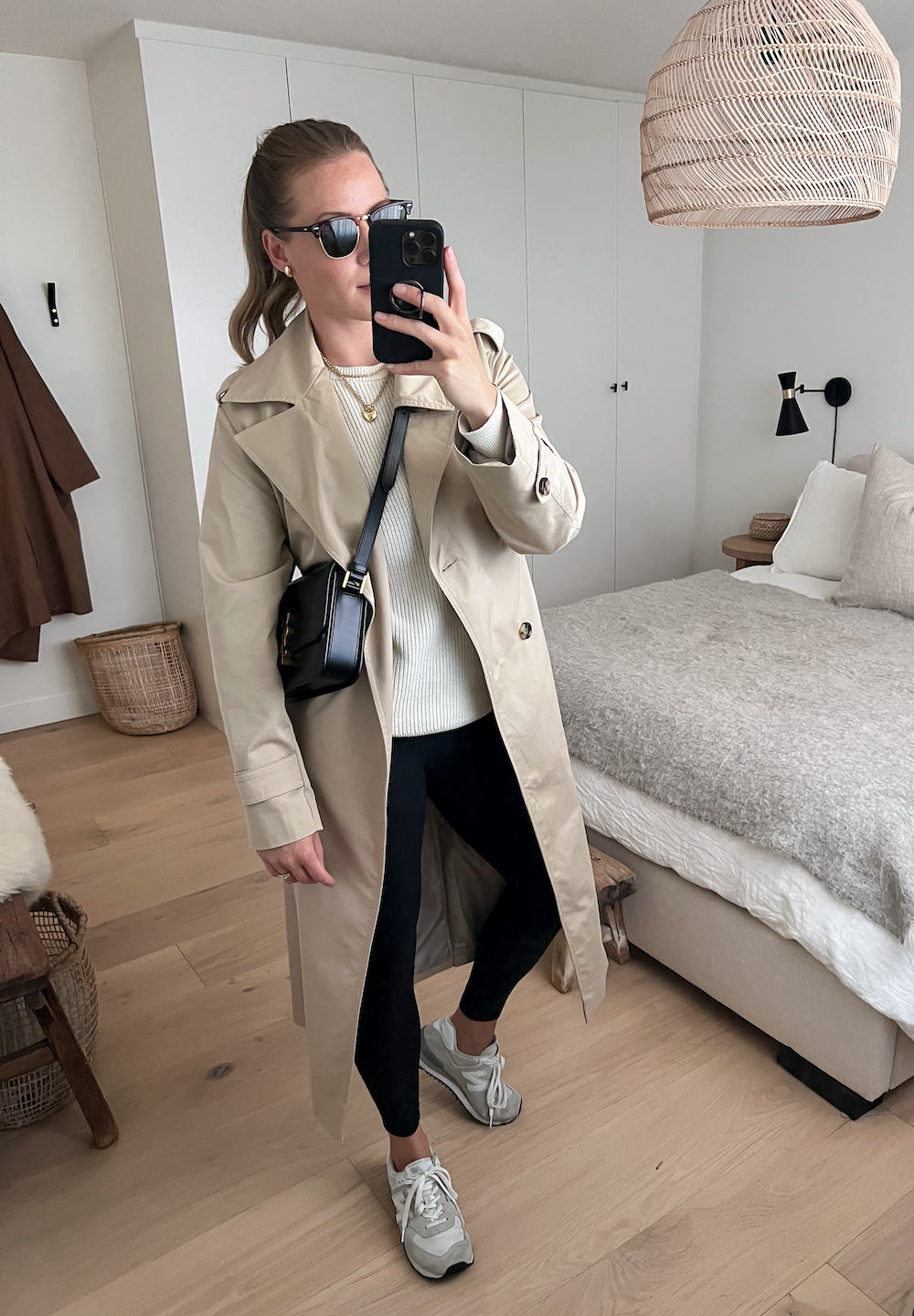 Christal wearing black leggings, a cream colored sweater, sneakers and a long tan trench coat.