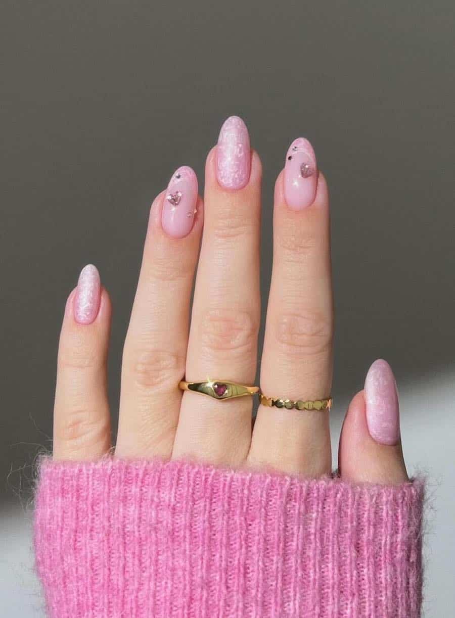 Medium almond nails with pink pearly polish and French tip accent nails with pink heart-shaped gems