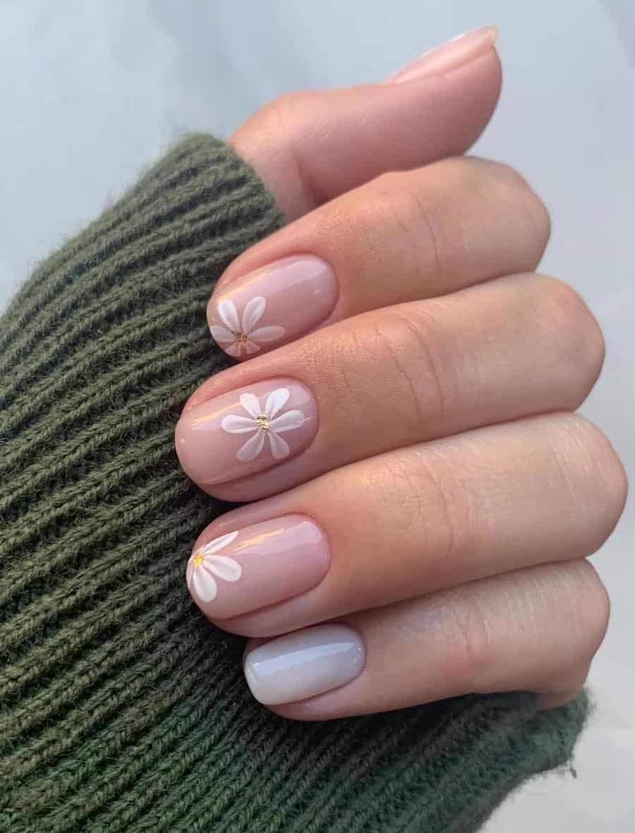 Short round nude nails with simple white flowers and gold foil centers and one milky white accent nail
