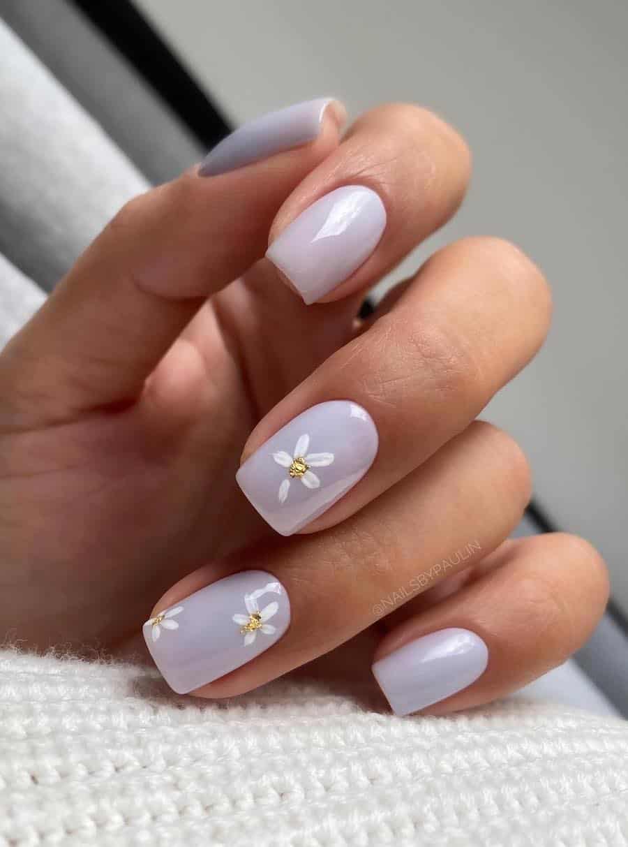 Short square nails with pastel purple polish and accent nails featuring white flowers with gold foiol centers