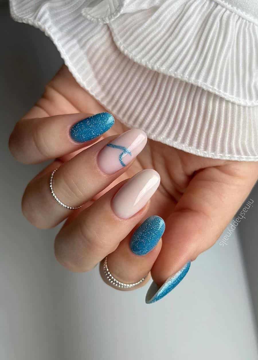 Medium round nails with glittering blue nail polish and two milky white accent nails, one featuring a glittering blue wave