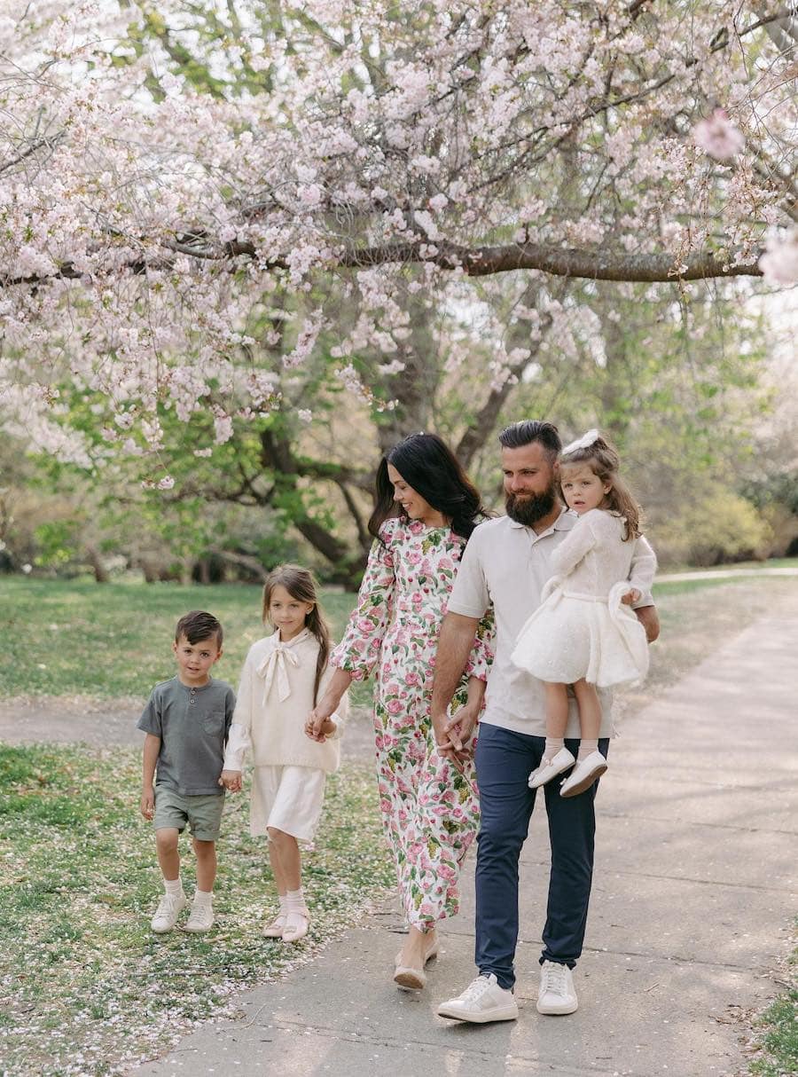 A spring family photo for a family of 5 featuring a floral dress on the mom, white outfits for the daughters, and short sleeved tees for the father and son
