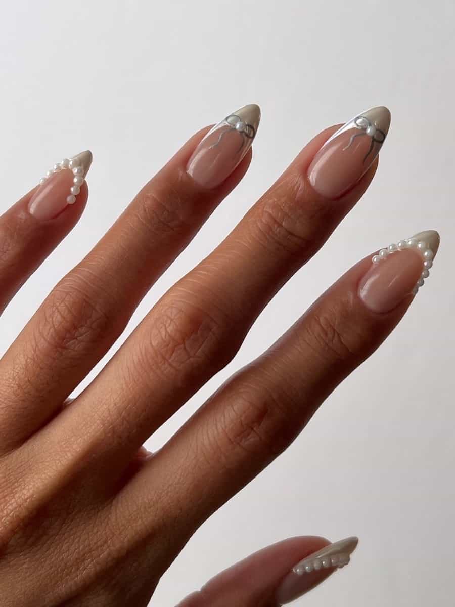 Medium nude almond nails with silver tips accented with silver bows and white pearls