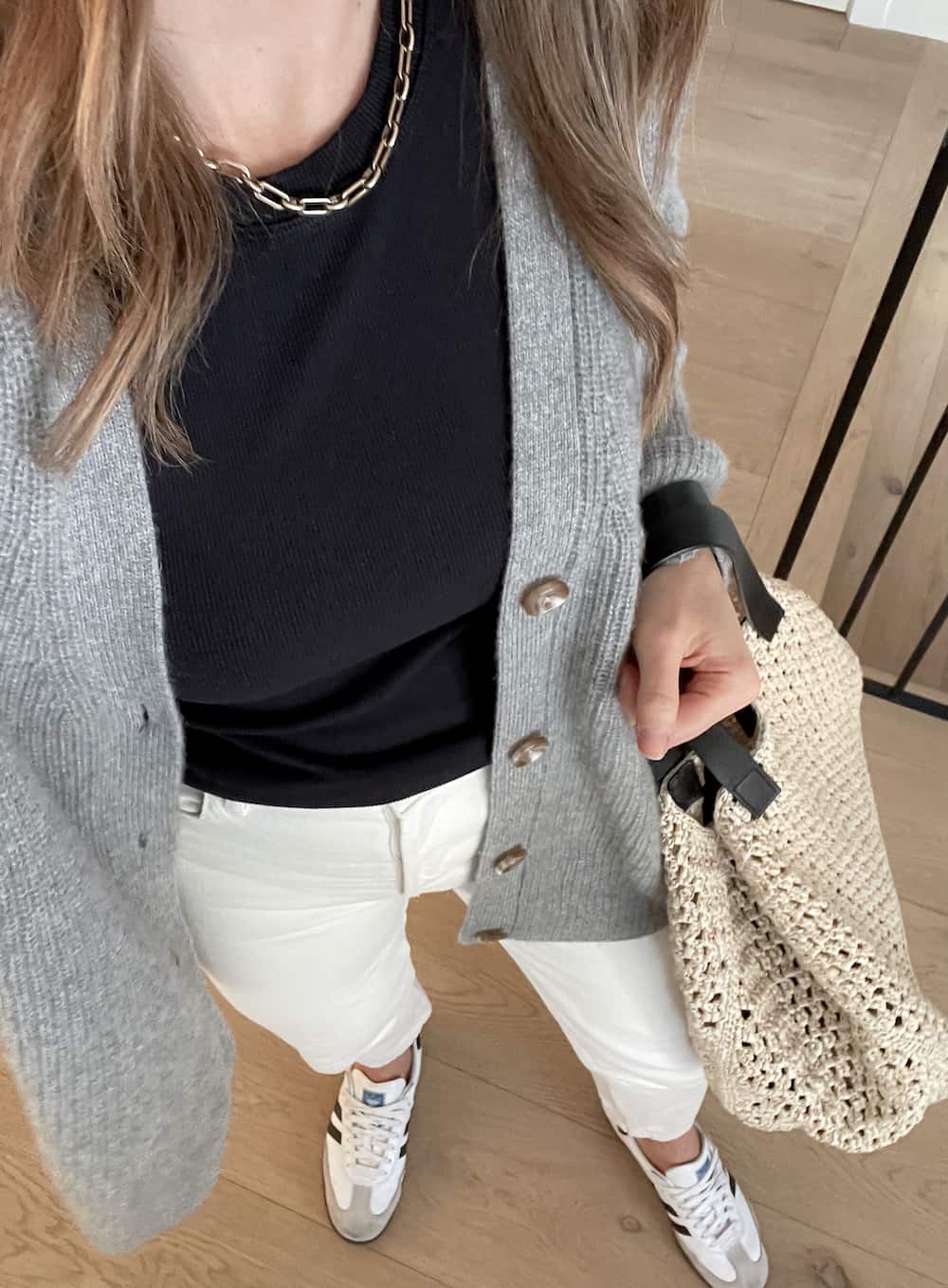 Christal wearing white jeans, sneakers, a black t-shirt and a grey cardigan sweater.