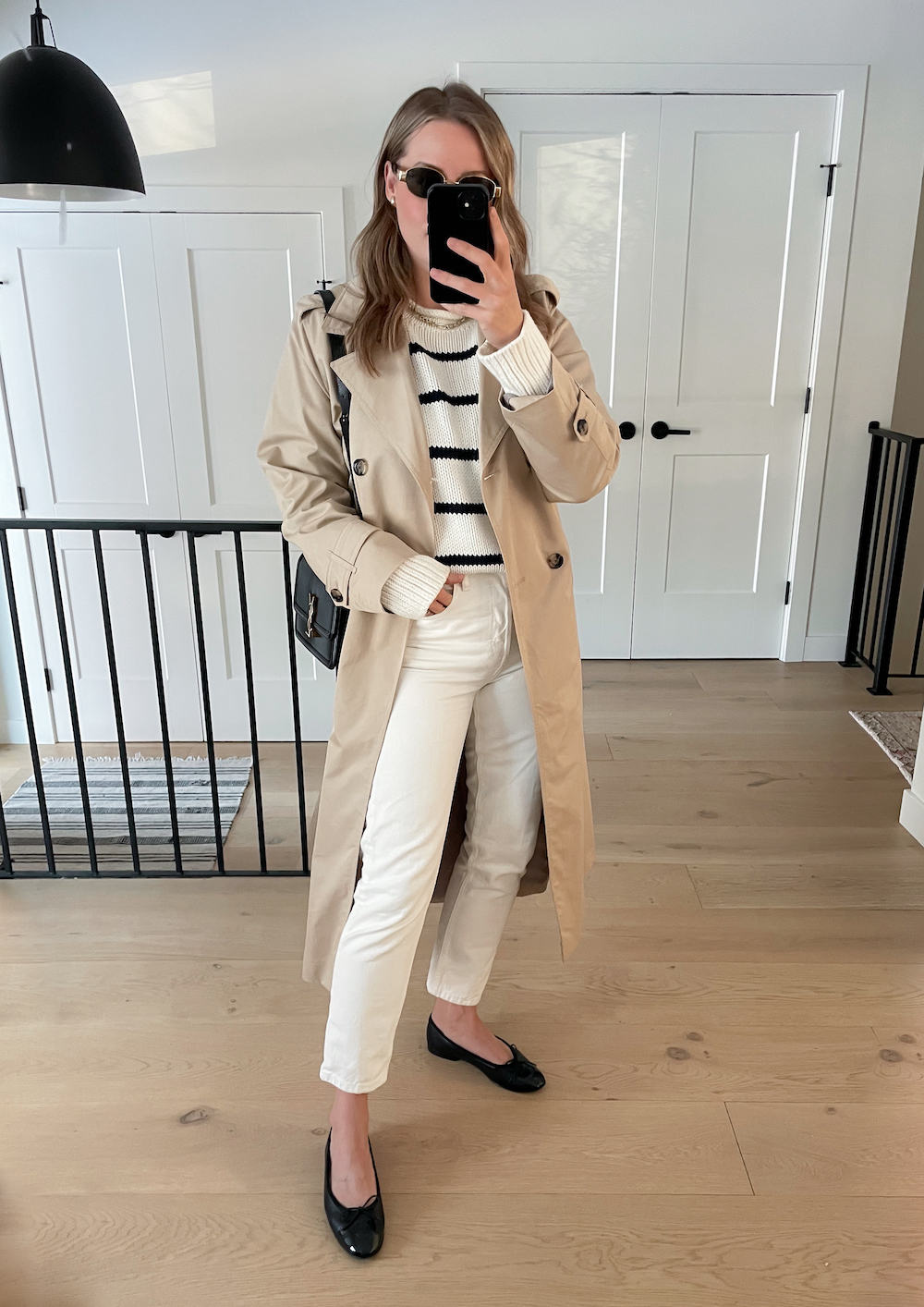 Christal wearing white jeans, black ballet flats, a black and white striped sweater and a tan trench coat.