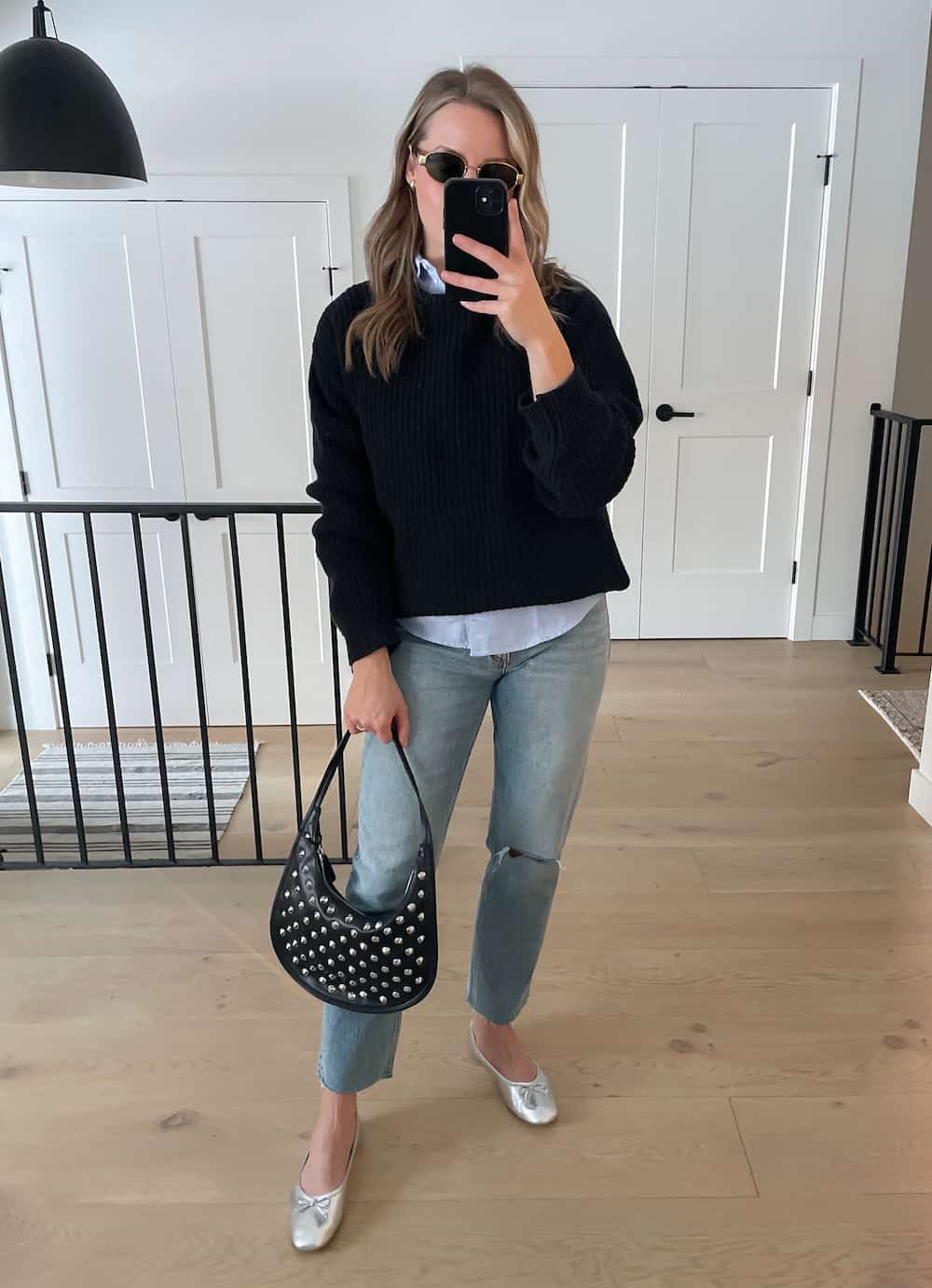 Christal wearing jeans, silver ballet flats and a blue button down under a black sweater with black accessories.