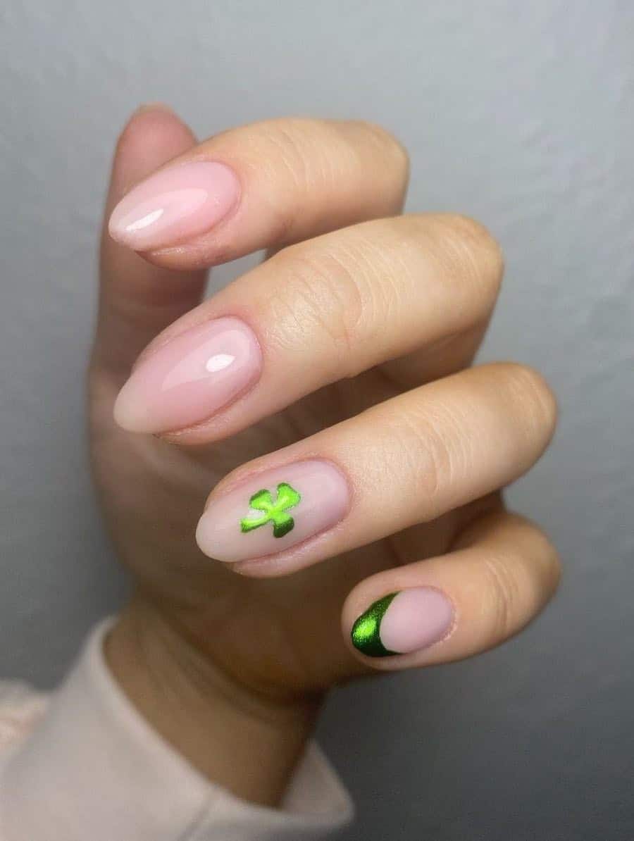 Short pink nude almond nails and two accent nails, one with a green chrome tip and the other with a green chrome three leaf clover
