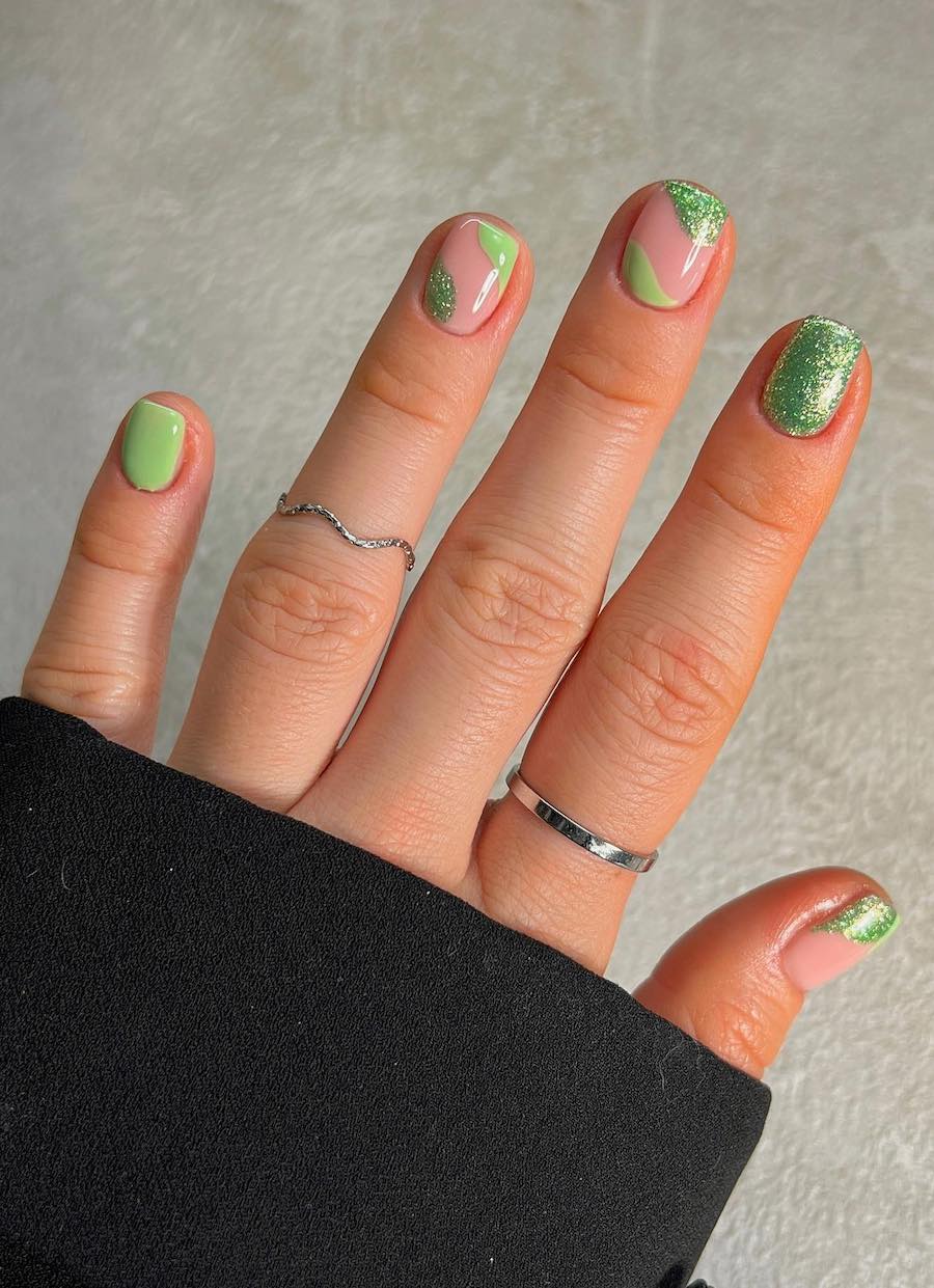 Short squoval nails with glittery green and lime green green nail polish and accent nails with wave details