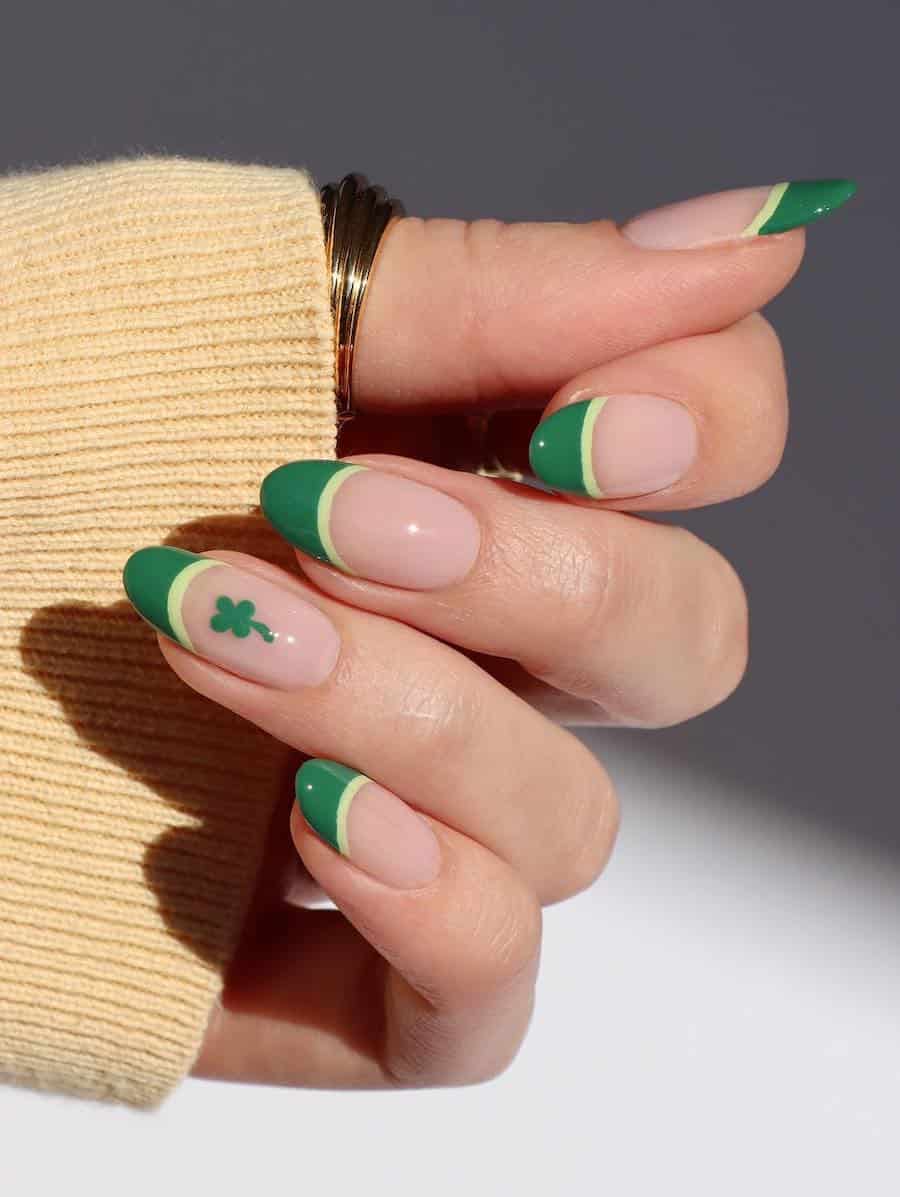 Medium nude almond nails with dark green French tips with light green borders and an accent nail with a four leaf clover