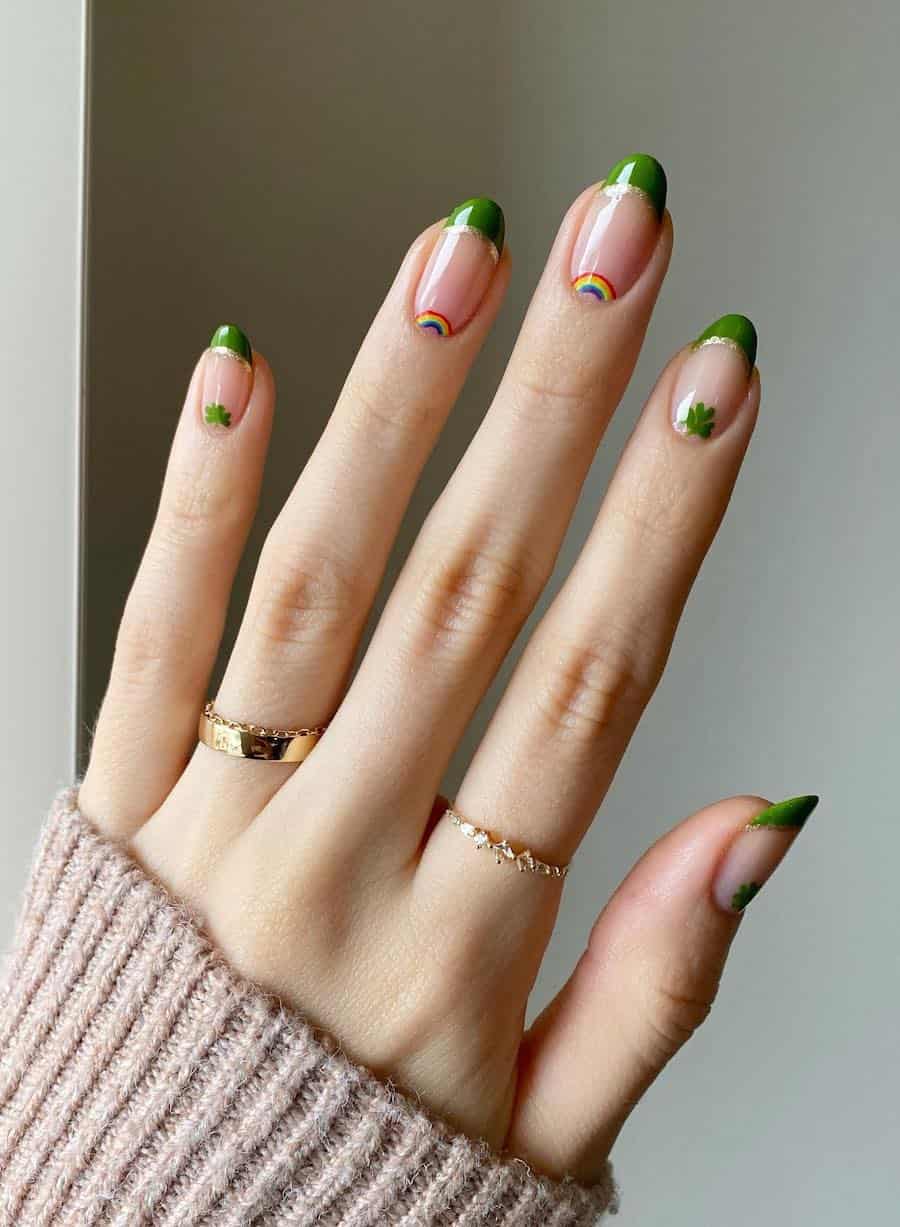 Short round nude nails with green and gold glitter tips with rainbow and clover nail art at the base