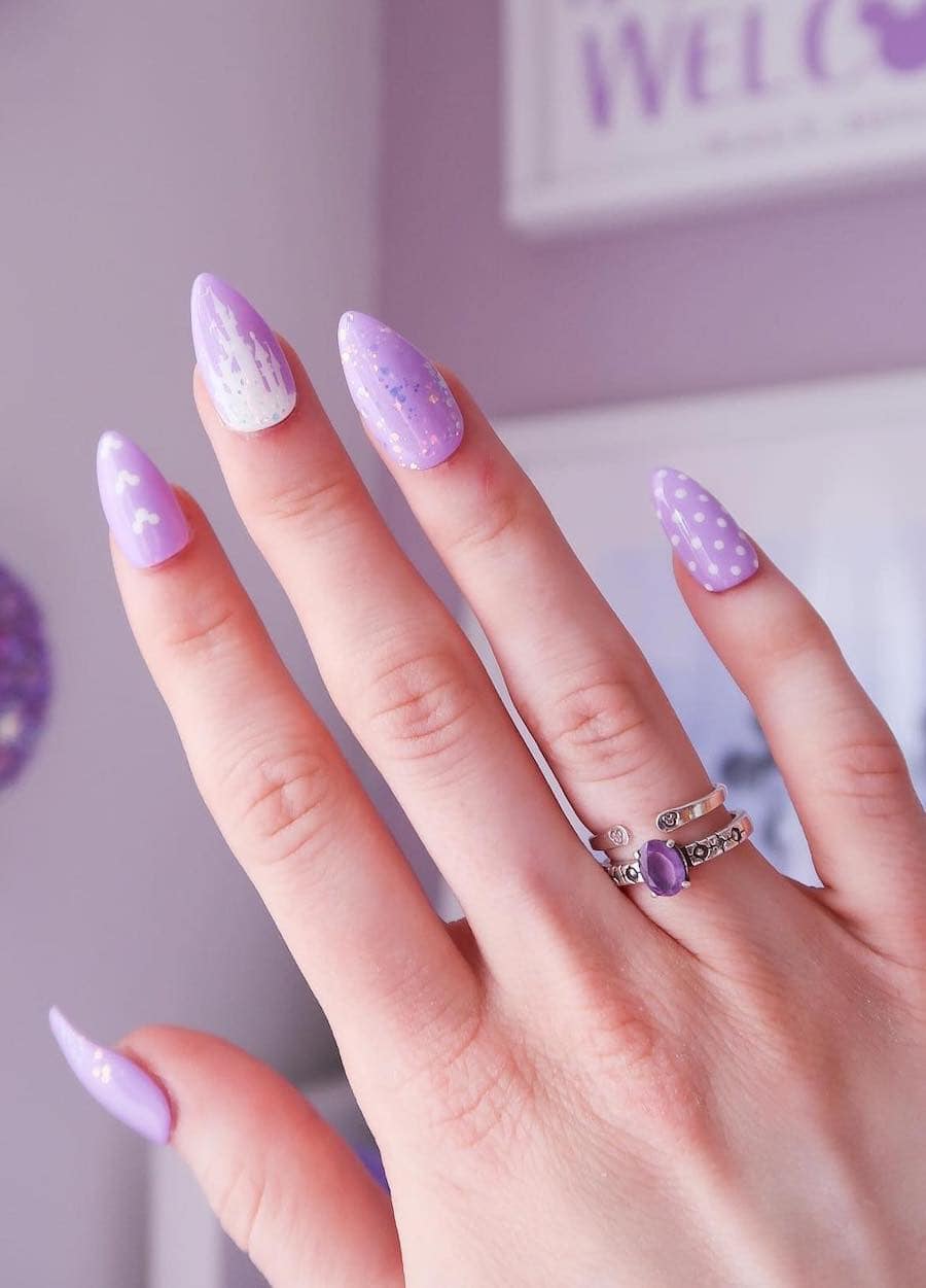 Medium almond nails with a Disney design featuring soft purple polish, glitter, and white nail art including the Disney castle
