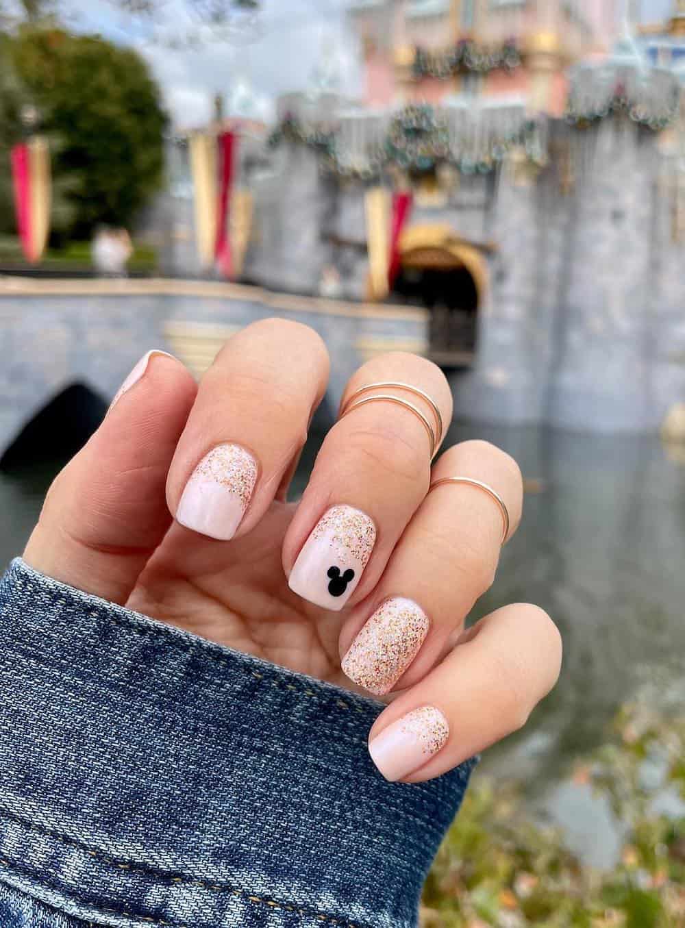 Short squoval nails with a Mickey Mouse design featuring nude pink and gold glitter