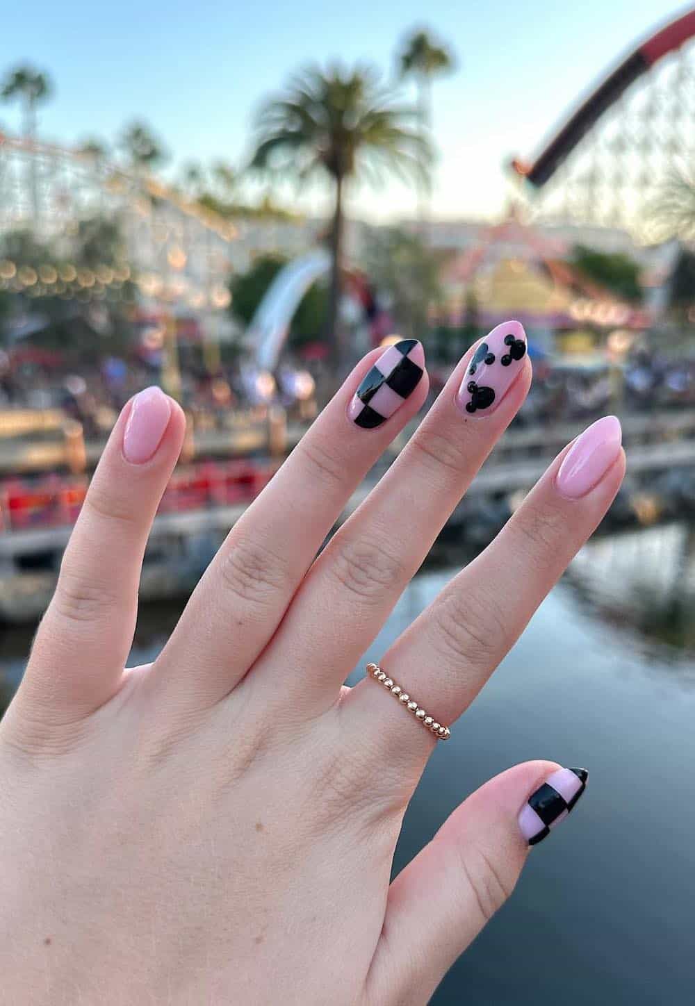 Medium almond nails with a Mickey Mouse design featuring nude pink and black polish with checkerboard print
